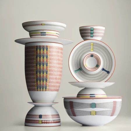 Stack of decorative porcelain dinnerware, including bowls and plates with geometric designs, against a pale neutral background.