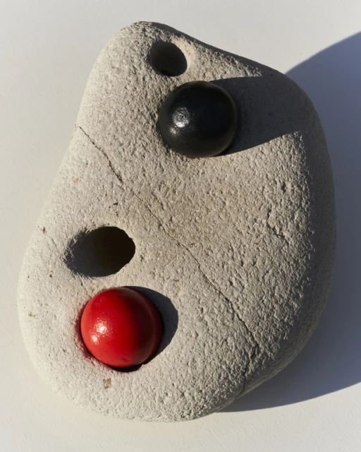 Stone with red and black balls inserted, textured surface, strong shadows, simple composition, natural material, close-up view.