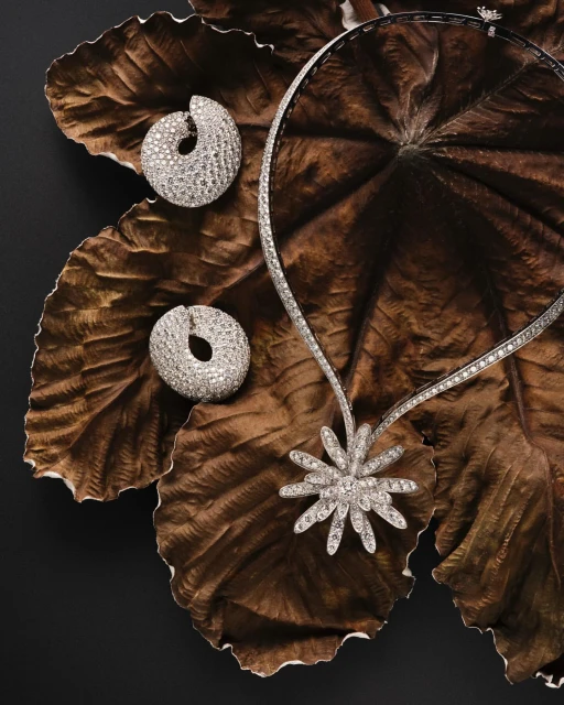 High-end jewelry on a textured leaf background: a diamond necklace with flower pendant and matching diamond stud earrings sparkle.