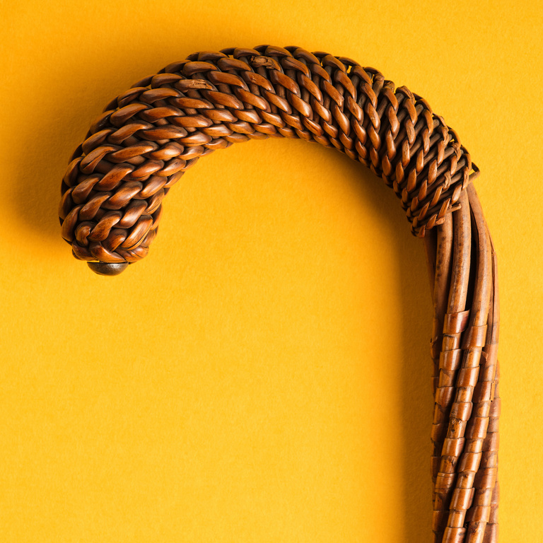 Close-up shot of a walking cane made of interwoven brown wicker on a solid yellow background.