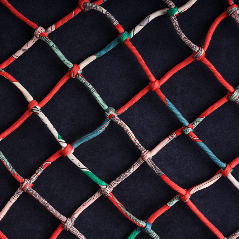 Abstract close-up of a knotted net in red, blue, white, and green against a dark background, showcasing a unique textile design.