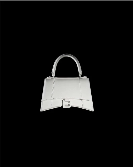 Silver Balenciaga handbag isolated on a stark black background, showcasing its trapezoidal design, handle, and the distinctive B logo.