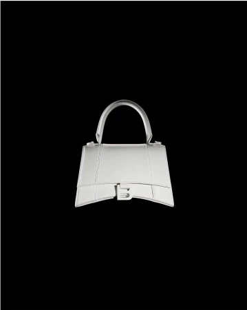 Silver Balenciaga handbag isolated on a stark black background, showcasing its trapezoidal design, handle, and the distinctive B logo.