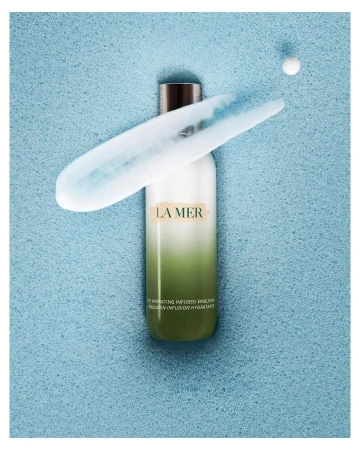 La Mer moisturizer on a blue textured background with a streak of moisturizer and single pearl near the top right corner of the frame.