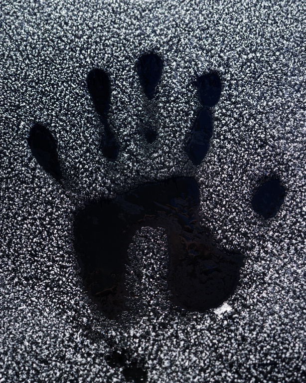 Close-up of a black handprint impression on a frost-covered surface. The frost creates a textured backdrop, highlighting the hand silhouette.