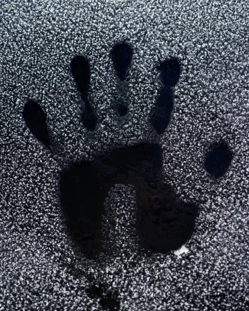 Close-up of a black handprint impression on a frost-covered surface. The frost creates a textured backdrop, highlighting the hand silhouette.