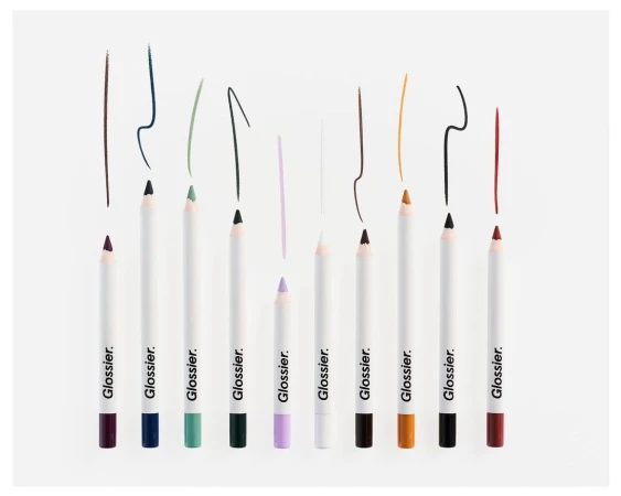 Cosmetic still life featuring a lineup of colorful Glossier eye pencils with matching colored pencil strokes, against a white backdrop.