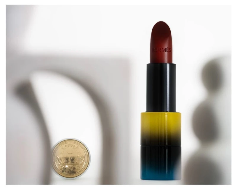 Still life shot of opened Hermes lipstick with a gold coin in the background, showing luxury beauty and cosmetic product photography.