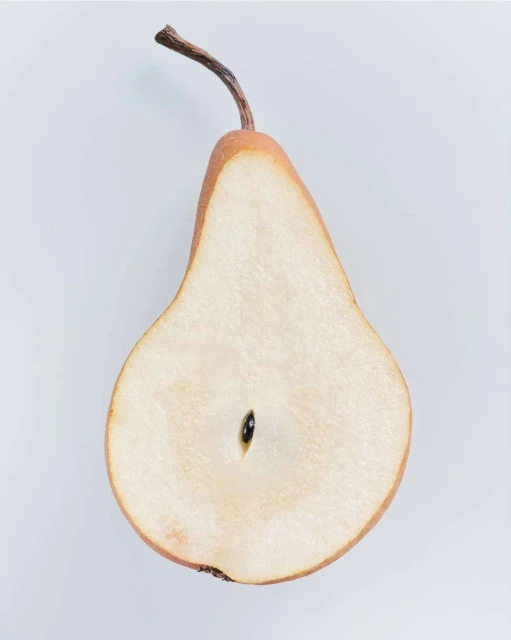 Close-up of a halved pear revealing its inner texture, seed, and stem against a soft white background, highlighting the fruit's natural detail.