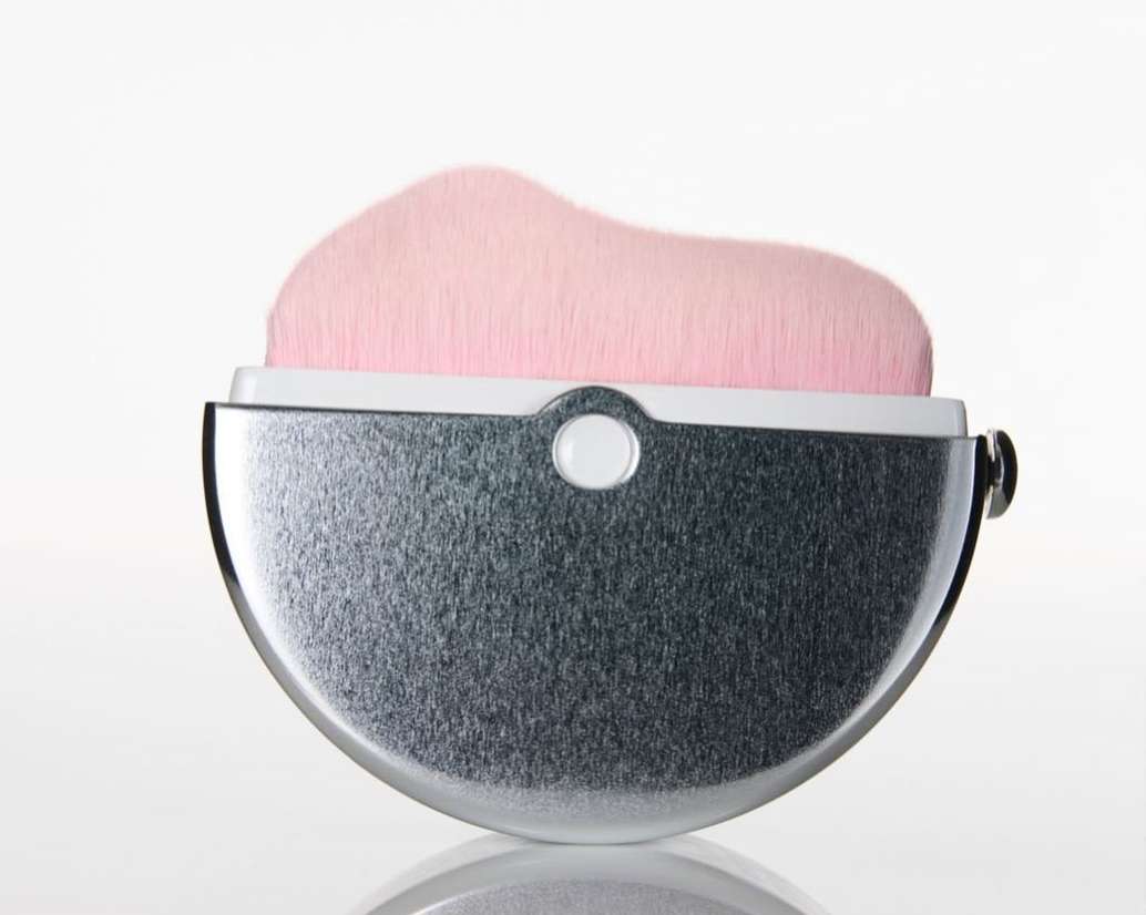 Close-up studio shot of a silver and white makeup brush with soft pink bristles. Isolated on a seamless white background.