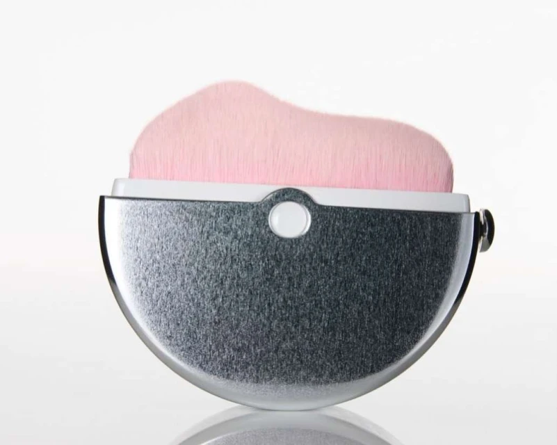 Close-up studio shot of a silver and white makeup brush with soft pink bristles. Isolated on a seamless white background.