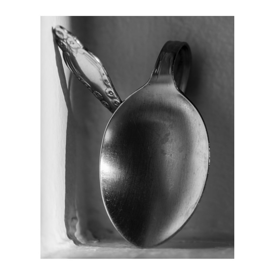 Black and white still life photograph featuring two silver spoons with curved handles, positioned close together with soft, neutral background.