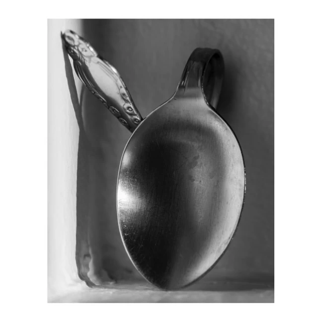 Black and white still life photograph featuring two silver spoons with curved handles, positioned close together with soft, neutral background.