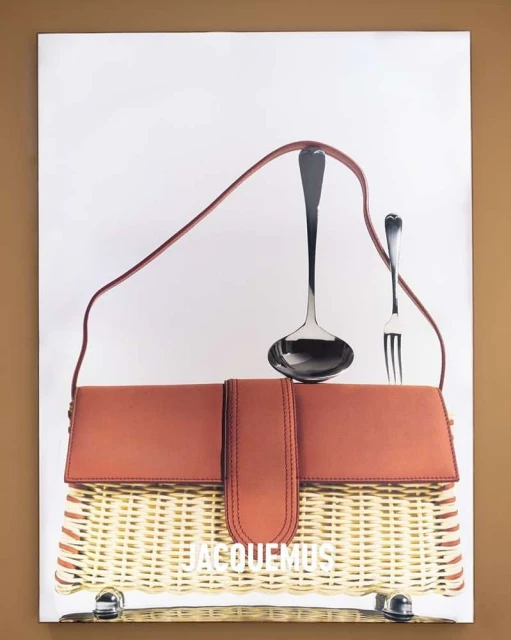 Promotional product shot featuring a brown and tan wicker handbag with a brown strap, accompanied by a large silver ladle and fork.