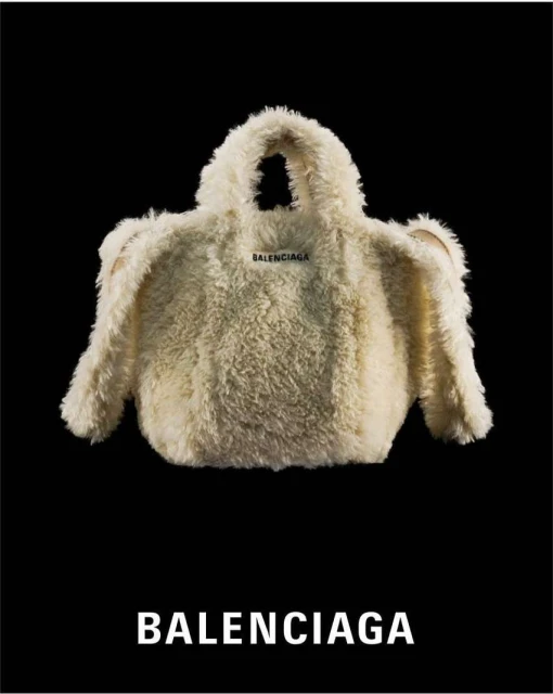 Ivory-colored Balenciaga handbag, made from faux fur fabric with handles, showcased against a black background, featuring a brand logo.