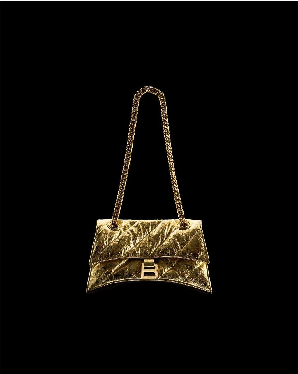 Gold Balenciaga purse with chain strap on a black backdrop. Metallic, shimmering material with a distinctive 'B' logo clasp.