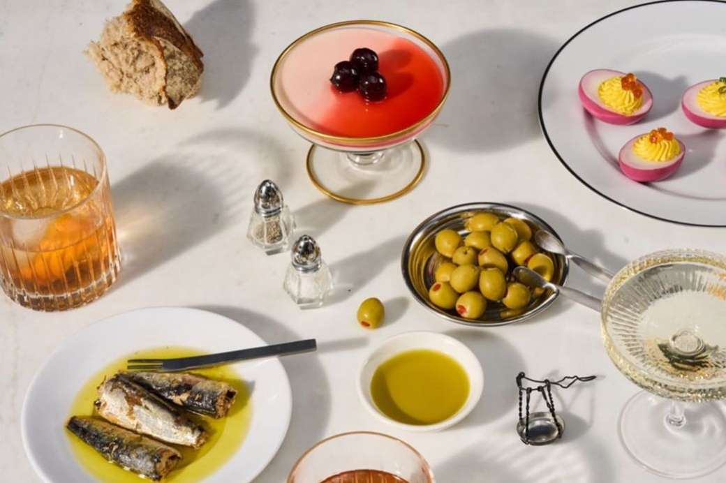 Overhead shot of a table arrangement featuring cocktails, deviled eggs, olives, and canned fish with warm lighting, inviting culinary presentation.