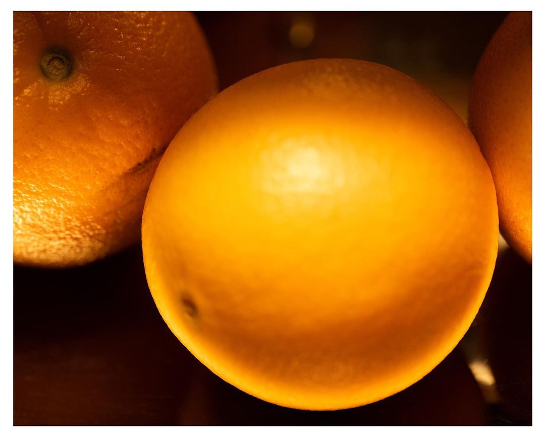 Close-up of multiple oranges with bright, yellow-orange peels, set against a dark background, showcasing texture and color.