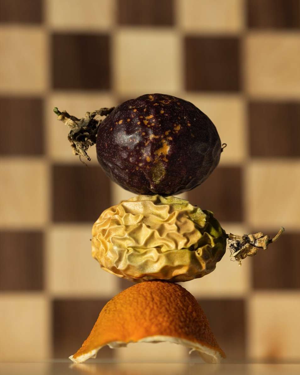 A stack of passion fruit and orange peel sits on a white surface, showcased against a checkered background in a studio setting.