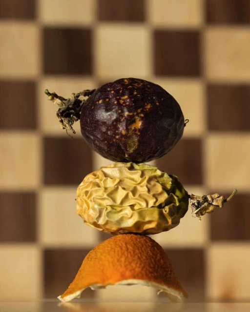 A stack of passion fruit and orange peel sits on a white surface, showcased against a checkered background in a studio setting.