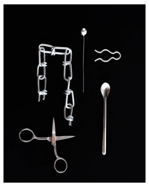 Still life of a silver chain, hairpin, stickpin, spoon, and scissors against a black background, showcasing metal objects.