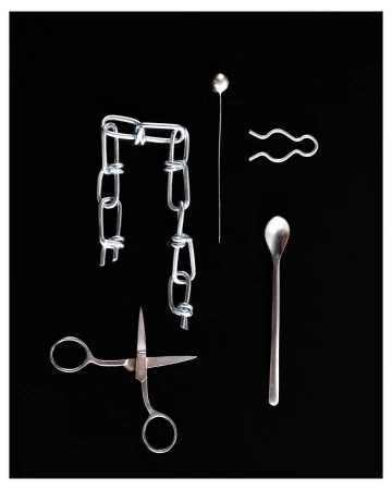 Still life of a silver chain, hairpin, stickpin, spoon, and scissors against a black background, showcasing metal objects.