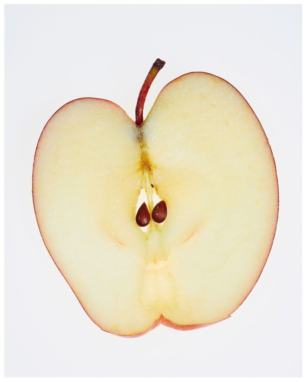 Close-up of a halved red apple on a white background, showcasing its seeds, stem, and the juicy interior of the fruit.