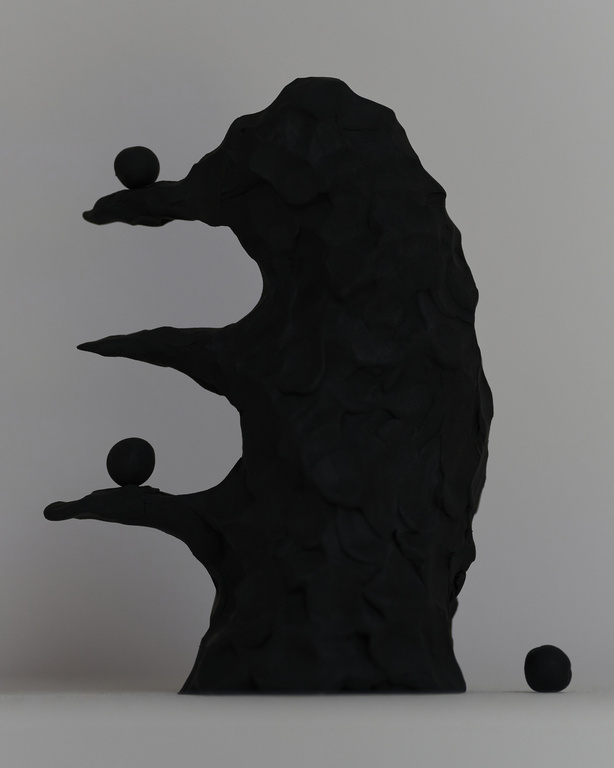 Abstract sculpture featuring a textured black tree-like structure with three spherical objects on its branches, set against a grey backdrop.