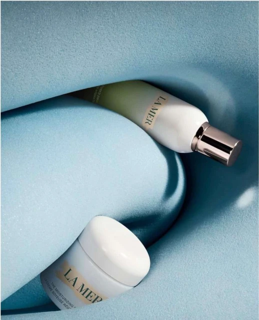 La Mer moisturizing cream and lotion in a pastel blue setting, product shot for the beauty and skincare industry.