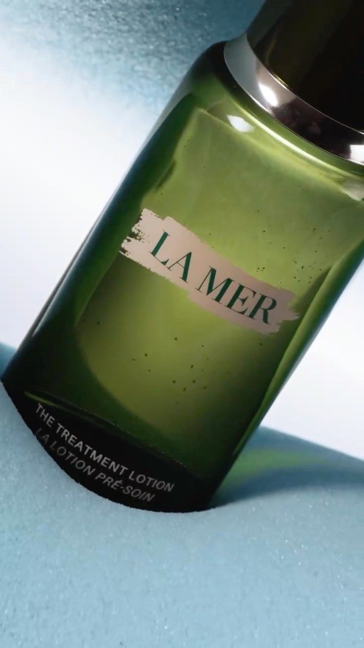 A bottle of La Mer The Treatment Lotion angled on a light blue surface, highlighting its packaging and product details.