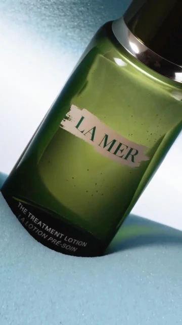 A bottle of La Mer The Treatment Lotion angled on a light blue surface, highlighting its packaging and product details.