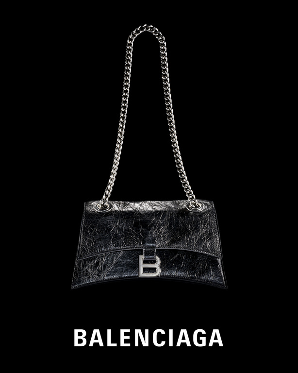 Balenciaga black leather handbag with silver chain straps and silver B logo against a black backdrop in a studio shot.