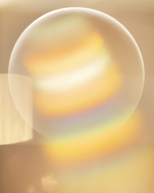 Abstract golden-toned image featuring a transparent sphere reflecting rainbow colors, casting soft light and lens flares on the backdrop.