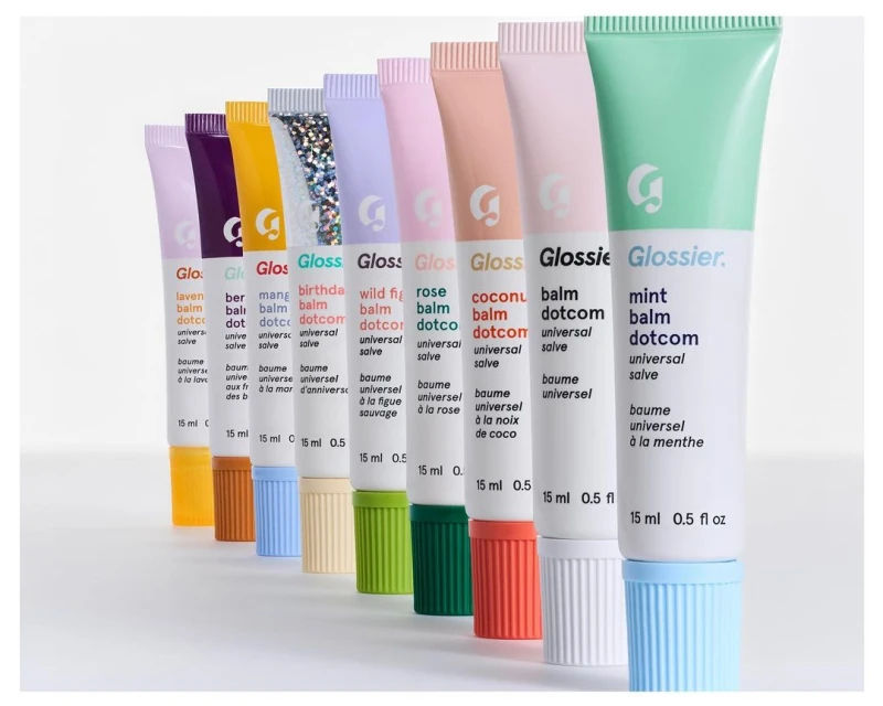 Glossier Balm Dotcom collection: multiple tubes of lip balm in various colors arranged in a row against a clean, white backdrop.