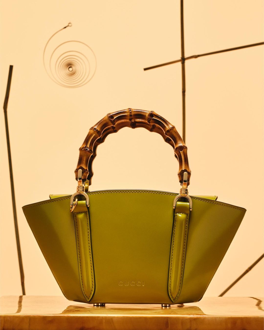 Gucci handbag in green with bamboo handle. Studio product shot against a tan background with natural bamboo decorations.
