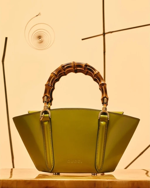 Gucci handbag in green with bamboo handle. Studio product shot against a tan background with natural bamboo decorations.