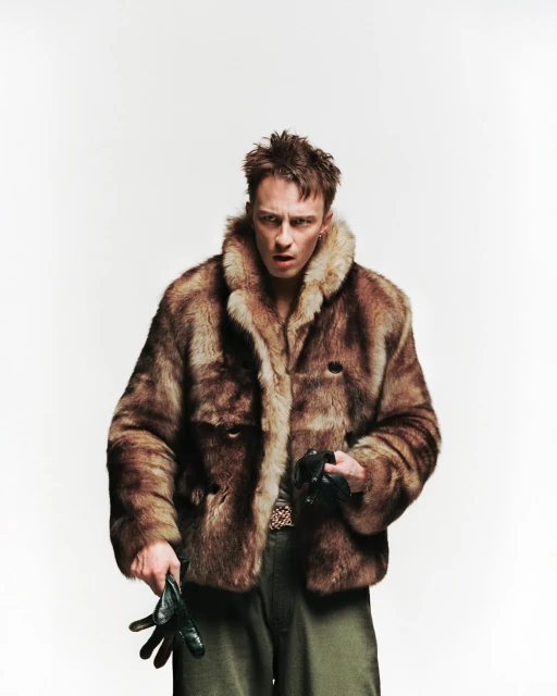 Portrait of a man in a fur coat holding leather gloves against a plain white backdrop, creating a dramatic and vintage fashion statement.