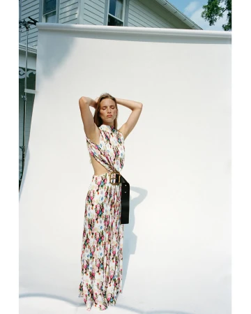 A woman posing in a floral print maxi dress with a wide black belt against a white seamless backdrop.