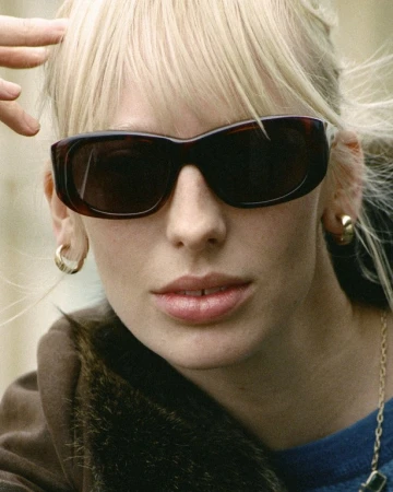 Close-up portrait of a blonde woman wearing tortoiseshell sunglasses and gold hoop earrings by photographer Thistle Brown.
