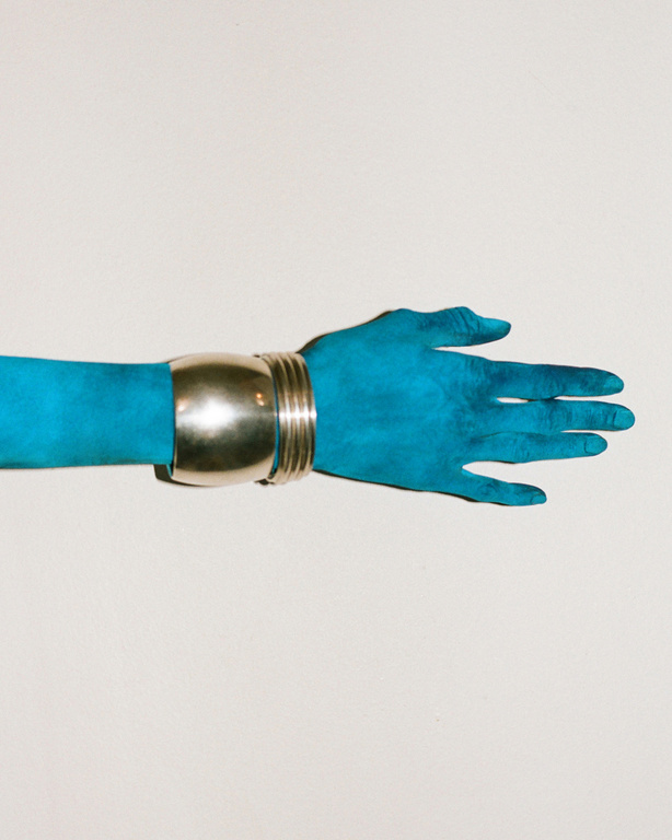A turquoise arm extends horizontally across a white background, adorned with a thick, metallic silver cuff bracelet around the wrist.