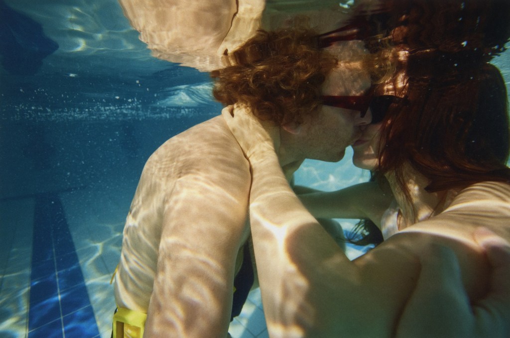 Underwater shot of a couple embracing in a swimming pool, captured in a close-up with bright lighting and clear water visibility.