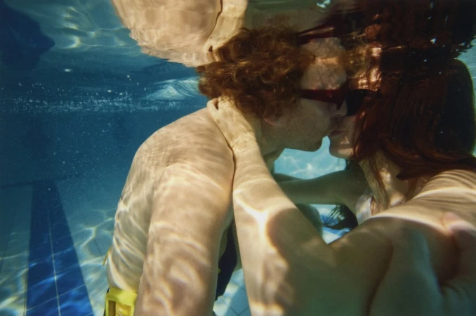 Underwater shot of a couple embracing in a swimming pool, captured in a close-up with bright lighting and clear water visibility.