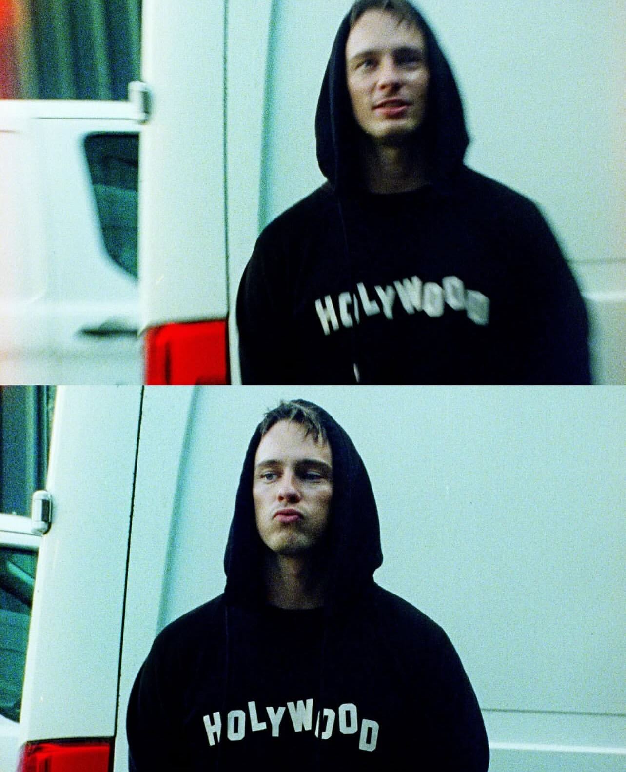 Man in hooded sweatshirt with Hollywood text, standing outside by a white van, expression is serious in the lower frame, smiling above.
