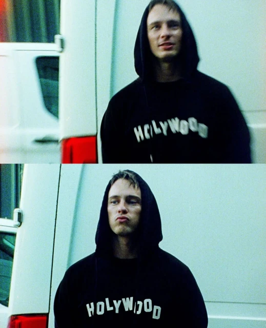 Man in hooded sweatshirt with Hollywood text, standing outside by a white van, expression is serious in the lower frame, smiling above.