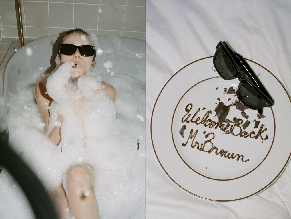 A woman in sunglasses is in a bubble-filled bathtub, alongside a dessert plate with 'Welcome Back Mr. Brown' written in chocolate.