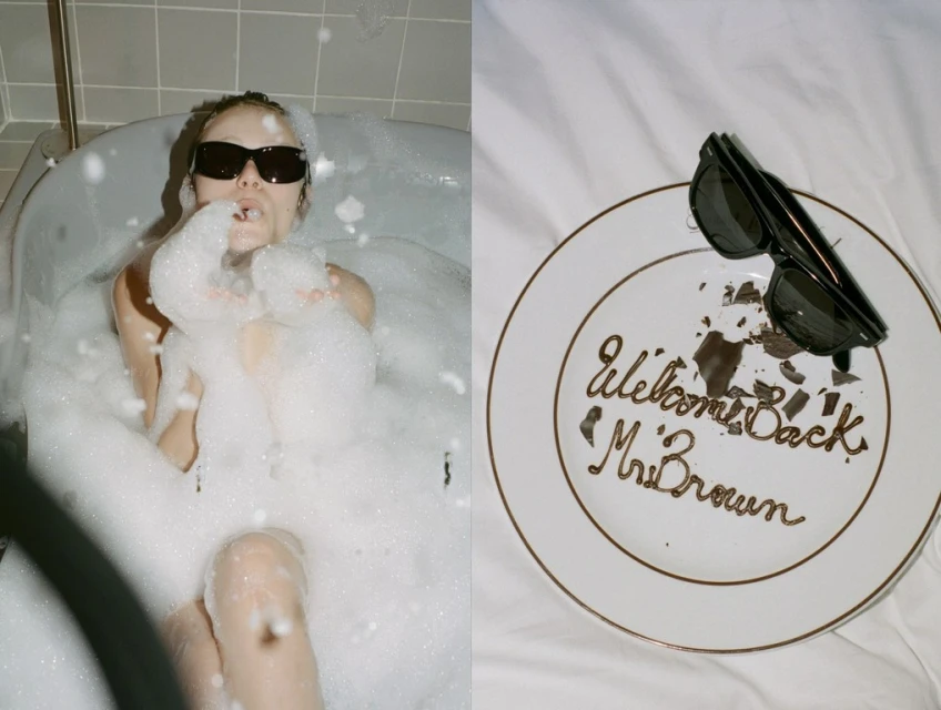 A woman in sunglasses is in a bubble-filled bathtub, alongside a dessert plate with 'Welcome Back Mr. Brown' written in chocolate.