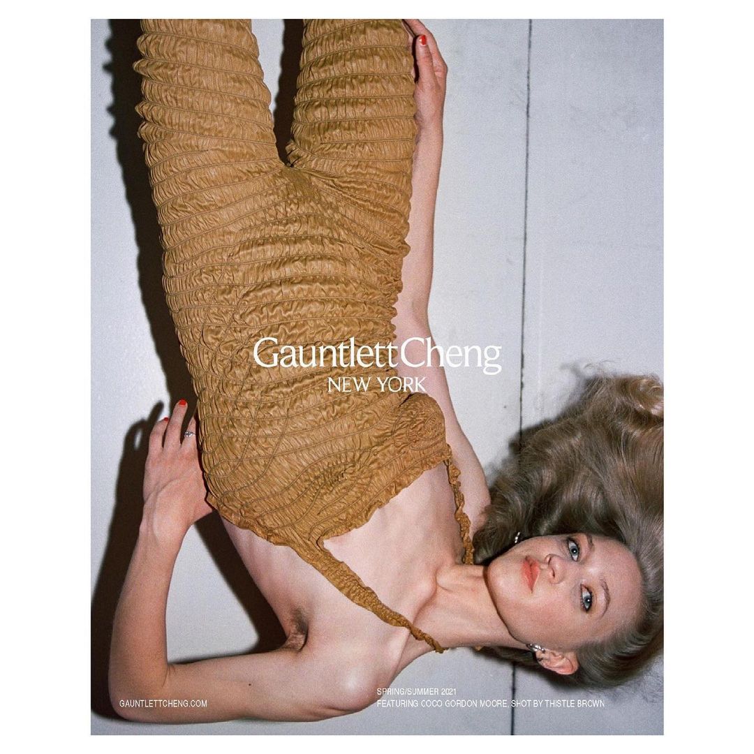 Fashion shot featuring a blonde woman in a tan textured outfit, posing on a neutral surface, bathed in soft, diffused light.