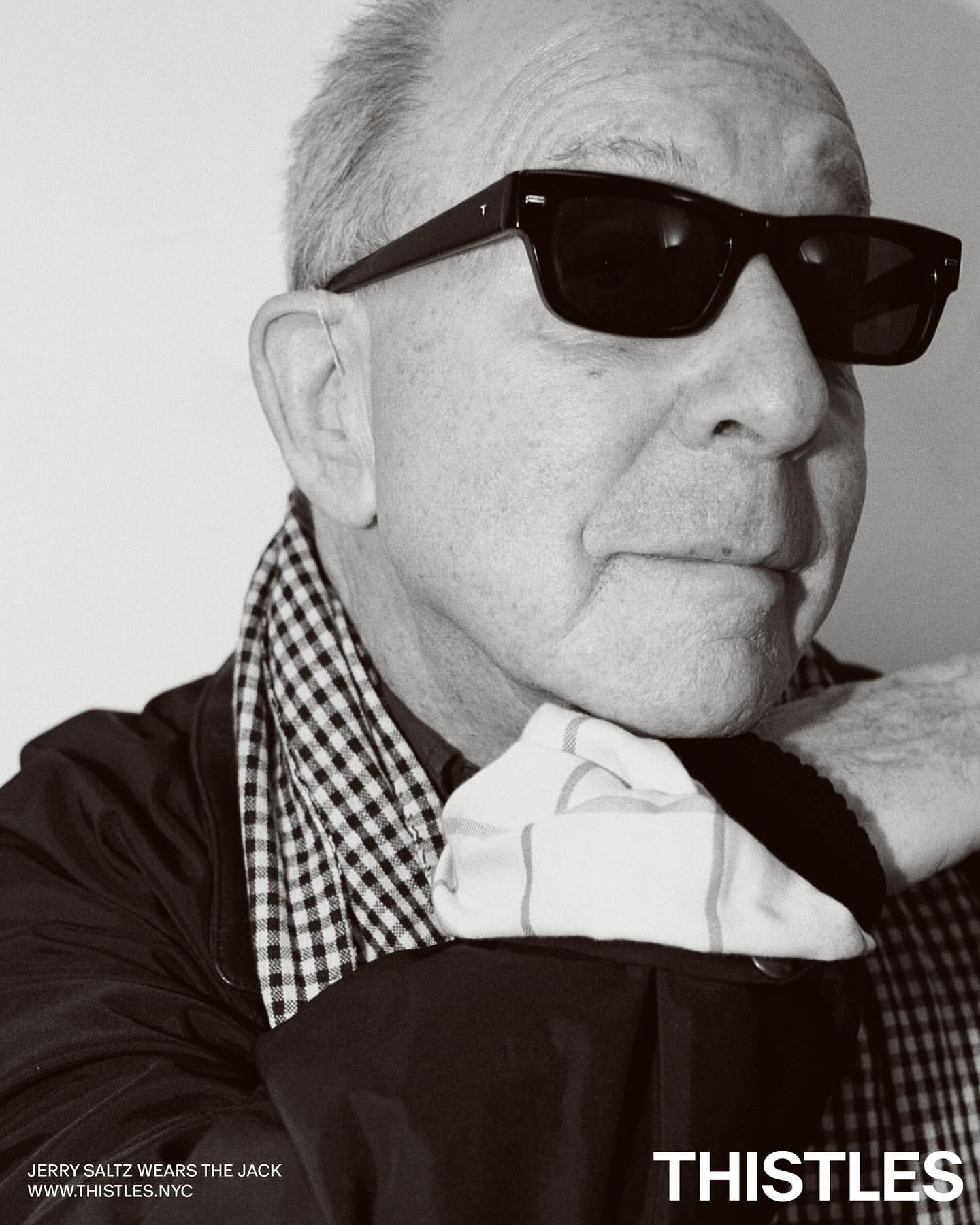 Portrait of Jerry Saltz wearing sunglasses and a checkered scarf. The image is black and white, with the brand THISTLES visible.