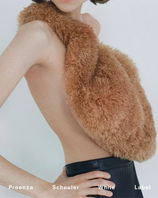 Fashion shot of a slender adult female model wearing a fluffy brown scarf, posing in front of a plain white backdrop with visible brand logos.