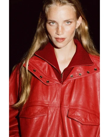 Portrait of a woman with long blonde hair and freckles wearing a red leather jacket and dark red zip sweater by Thistle Brown.